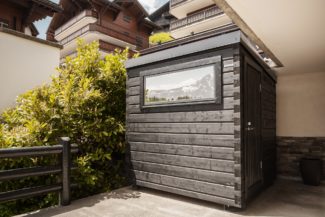 Sauna cube en bois avec petite fenêtre réfléchissante installé sur un balcon.
