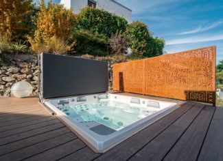 Spa intégré dans une terrasse en bois avec barrière en acier corten par Nicollier